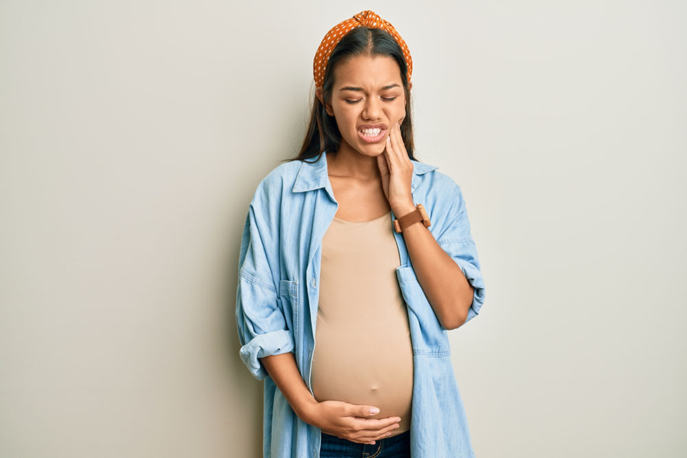 Беременная женщина держится за живот и зубы