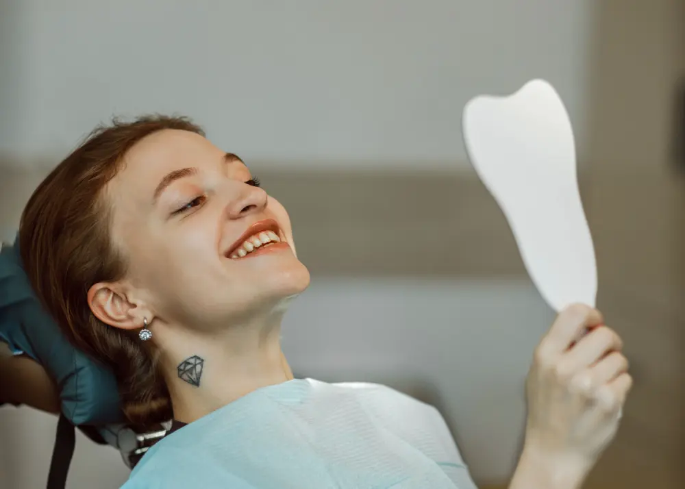 Девушка смотрит в зеркало на зубы после чистки у стоматолога