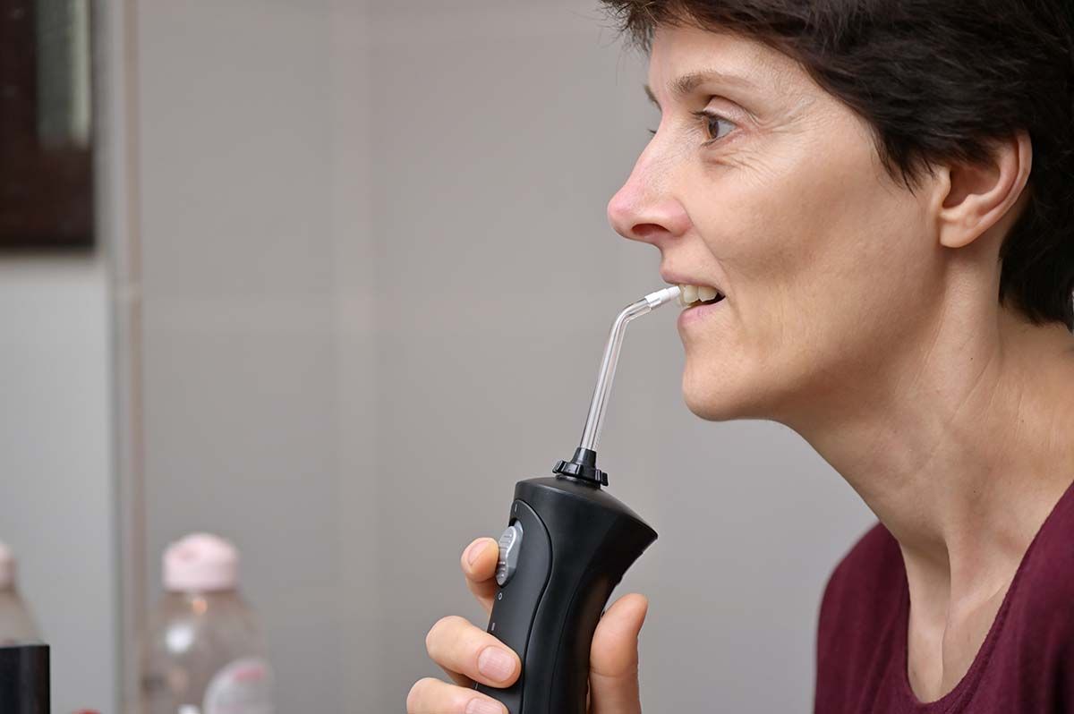 Женщина средних лет использует ирригатор для ухода за зубными имплантами